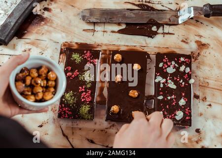 top view of chocolatier adding caramelized hazelnuts in dark chocolate bar Stock Photo