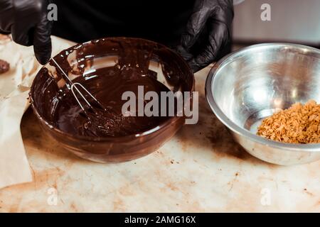 cropped view of chocolatier in black latex gloves whisking melted chocolate Stock Photo