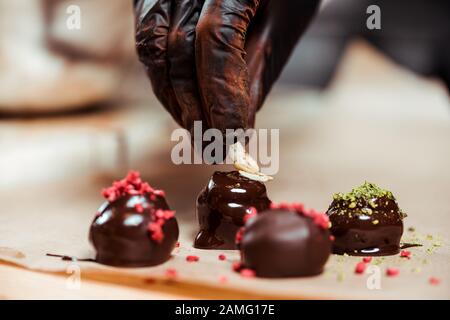 cropped view of chocolatier in black latex glove adding nuts on fresh made candies Stock Photo