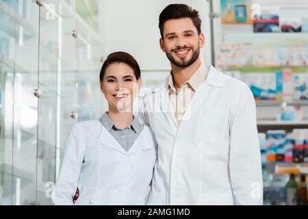 Pharmacists in white coats smiling at camera in pharmacy Stock Photo