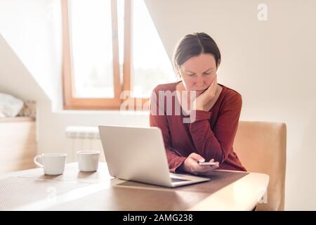 Woman telecommuting in home office interior. Portrait of female freelancer using mobile phone, selective focus. Stock Photo