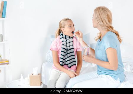 mother giving pill to sick daughter with opened mouth Stock Photo