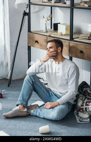 handsome and shocked man obscuring face in robbed apartment Stock Photo