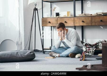 handsome and shocked man obscuring face in robbed apartment Stock Photo