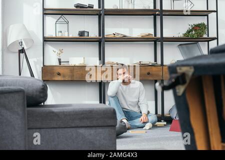 handsome and shocked man obscuring face in robbed apartment Stock Photo