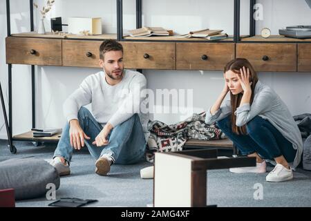 sad woman and handsome man sitting on floor in robbed apartment Stock Photo