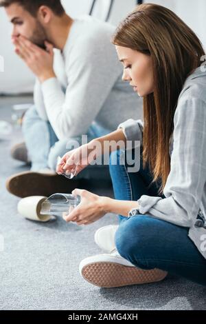 selective focus of attractive woman holding glass and shocked man on background in robbed apartment Stock Photo