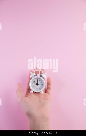 Pastel background with white alarm clock on pink background in hands with copy space. Stock Photo
