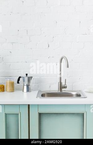 modern white and turquoise kitchen interior with kitchenware and sink near brick wall Stock Photo