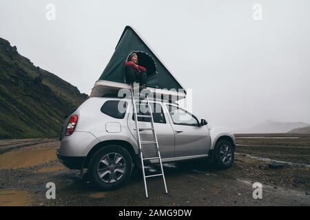 Landmannalaugar, Iceland - August 2018: Young woman sitting in autohome roof tent mounted on offroad car Stock Photo