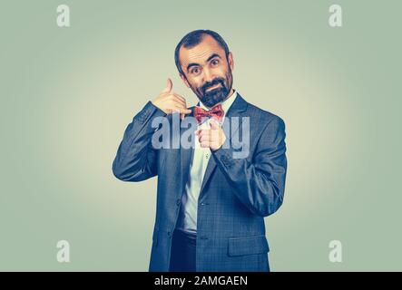 Standing bearded businessman shows call me gesture and pointing towards camera hands gesture. Isolated green yellow background. Human emotions face ex Stock Photo