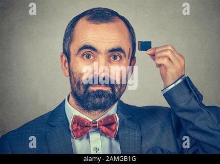 External memory needed concept. Portrait of a serious bearded businessman wearing elegant jacket and red bow tie holding Micro SD card near his head i Stock Photo