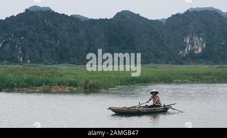 Ninh Binh, Vietnam - May 2019: Vietnamese woman in a wooden rowing boat going through Trang An nature park. Stock Photo