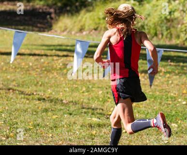 Rear view of a female high school cross country runner racing on the grass at the New York State Federation course in Bowdoin park. Stock Photo