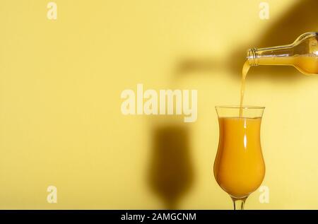 Orange juice poured from a bottle against a yellow background. Yellow monotone image with a fresh glass of orange juice. Summer refreshing drink. Stock Photo