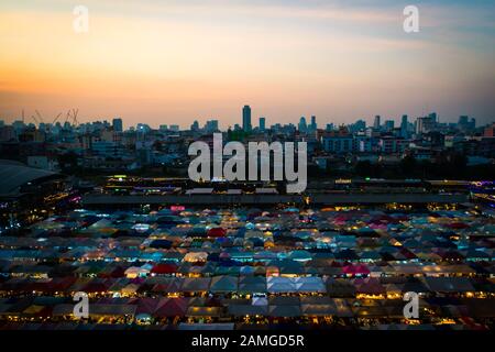 Bangkok/ Thailand - Decemebr 2019: View from the upstairs parking lot to the ratchada night market at sunset with the colorful stalls and Bangkok city Stock Photo