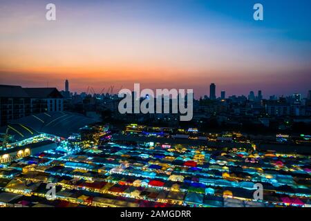 Bangkok/ Thailand - Decemebr 2019: View from the upstairs parking lot to the ratchada night market at sunset with the colorful stalls and Bangkok city Stock Photo