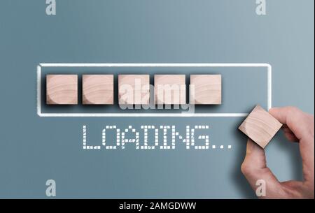 top view of hand holding wooden brick completing progress bar with text LOADING Stock Photo