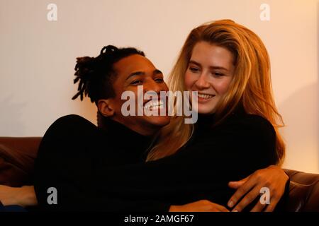 Young intercultural caucasian-hispanic student couple posing on sofa. Stock Photo