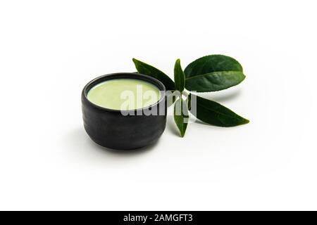 Hot green tea latte in black wooden bowl on white background. Place with deep Green tea leaves out side. Stock Photo