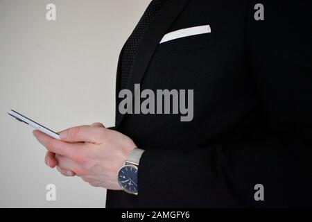 A close up view of a business man in a suit holding a smartphone Stock Photo