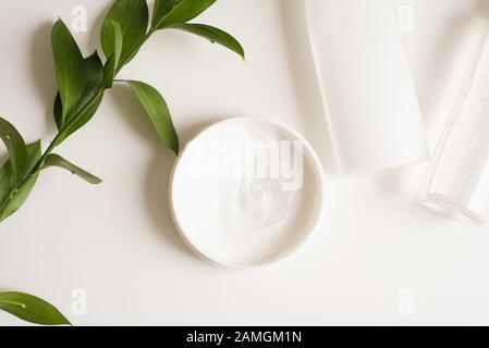 Means for skin care, rejuvenation and hydration of the face. Cream, micellar water and moisturizing lotion on a white background with a branch of gree Stock Photo