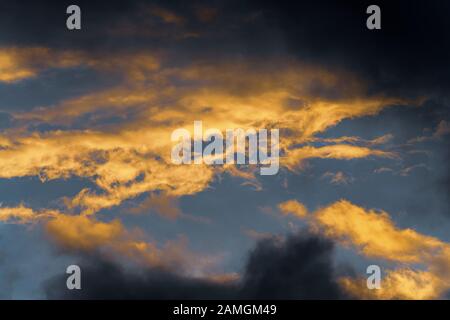 Stunning fluffy thunderstorm clouds illuminated by disappearing rays at sunset and dark thunderclouds floating across sunny blue sky to change season Stock Photo