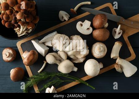 Different mushrooms, dill, bowl and board on wooden table, top view Stock Photo