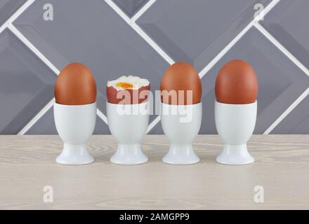 Four eggs in eggcups on wooden kitchen surface Stock Photo