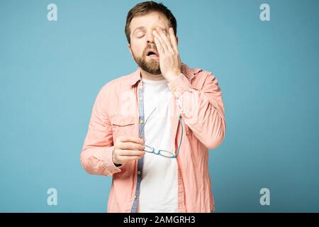 Very tired, sleepy man took off his glasses and rubs eyes with hand. Stock Photo
