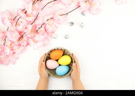 Child's hands holding basket with colored eggs on the Easter background. Stock Photo