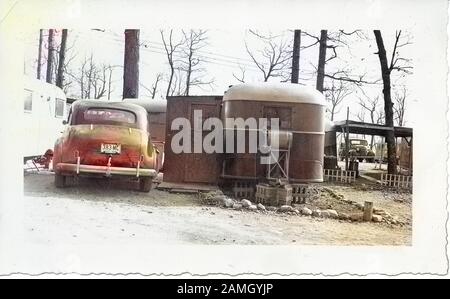 Black and white photograph, showing the back of a vintage Chevrolet sedan car, with an Ohio license plate dated 1945, parked outside, in a wintery landscape, next to a couple of caravans or towed trailers, likely photographed in Ohio in the decade following World War II, 1950. Note: Image has been digitally colorized using a modern process. Colors may not be period-accurate. () Stock Photo