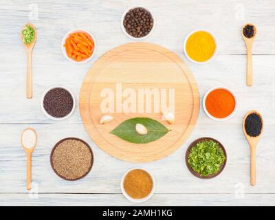 Round kitchen cutting board and ingredients for cooking: black pepper, turmeric, chili, green grass, masala, cumin (jeera), cardamom, carrot, dry onio Stock Photo