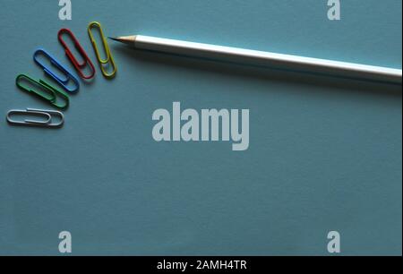 white wooden pencil and paper clips in different colors lying on a blue background Stock Photo