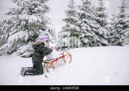 adorable girl having fun with snowman in snowy wonderland Stock Photo