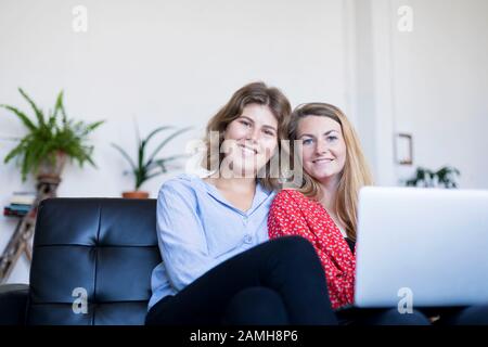 Two smiling young woman sitting on the sofa with laptop. Stock Photo