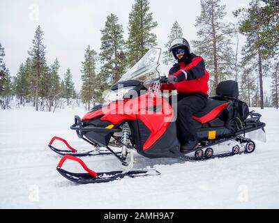 Happy smiling man driving snowmobile in Finnish Lapland Stock Photo