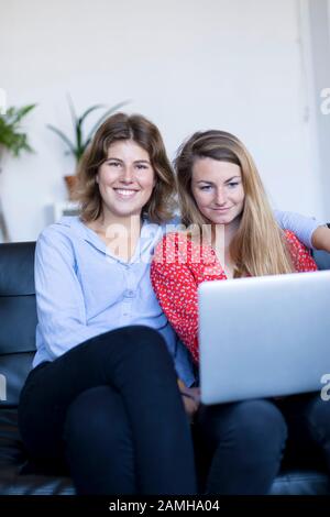 Two smiling young woman sitting on the sofa with laptop. Stock Photo