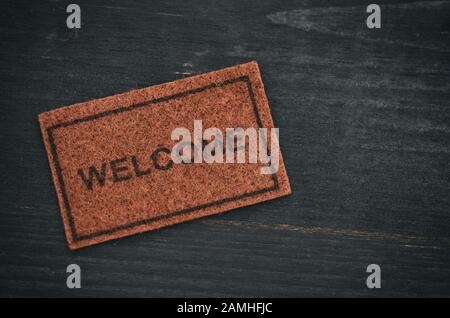 Old Welcome door mat on black wooden background, welcome concept, home concept Stock Photo