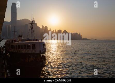 Hong Kong sunset; the sun setting over Hong Kong Island seen from the Star Ferry pier, Kowloon side, Hong Kong Asia Stock Photo
