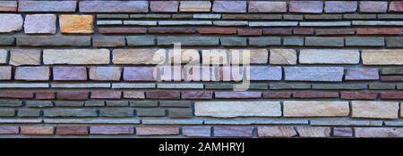 Multy-colored (colorful) decorative stone wall, texture, background. Varicolored flat stones of regular shape in the wall construction Stock Photo