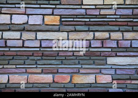 Multy-colored (colorful) decorative stone wall, texture, background. Varicolored flat stones of regular shape in the wall construction Stock Photo
