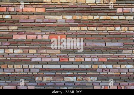 Multy-colored (colorful) decorative stone wall, texture, background. Varicolored flat stones of regular shape in the wall construction Stock Photo