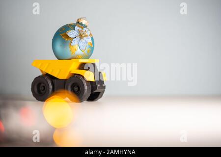 Yellow dump truck model with Christmas tree toy. Garland lights in defocus Stock Photo