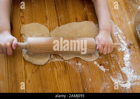 Hands of a boy rolling out dough on a wooden desk in a kitchen Stock Photo