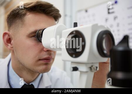 Close up portrait of male optometrist using refractometer machine while testing vision of unrecognizable patient Stock Photo