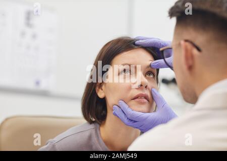 Back view portrait of young ophthalmologist opening eye of female patient while checking her vision in med clinic, copy space Stock Photo