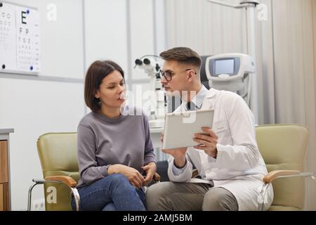 Portrait of young ophthalmologist using digital tablet while consulting female patient during eyesight check up in modern clinic, copy space Stock Photo