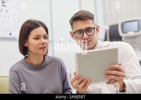 Portrait of young ophthalmologist using digital tablet while consulting female patient during eyesight check up in modern clinic Stock Photo