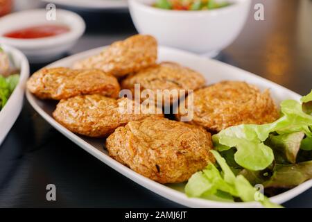 Thai Fried Fish Cake or Thai Deep fried fish pasty serve on white dish and black table. Stock Photo